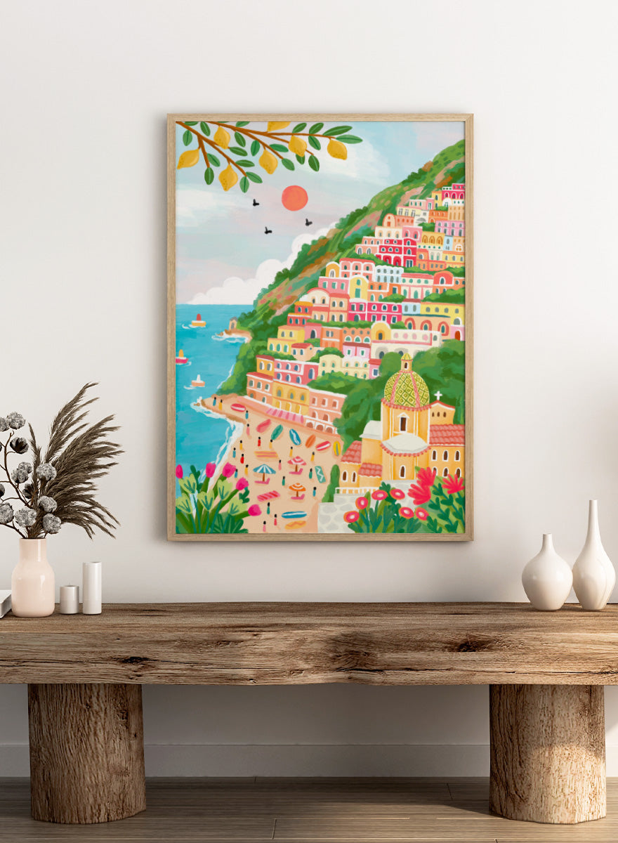 A colorful illustration of a coastal hillside town with tiered pastel buildings, a beach, blue sea, green foliage, and a church dome. Shop Vibrant Seaside Town by Nidhi Kachhadiya, a colorful coastal wall art print inspired by an Italian cliffside village, beach views, and bright Mediterranean color.