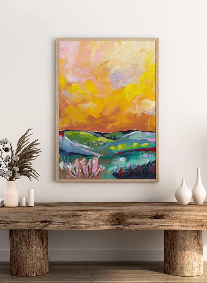 An abstract landscape painting featuring a dramatic yellow and orange sky over green and blue rolling hills, with textured brushstrokes. Shop Vibrant Sunset Landscape by Dirkie Nell, a colorful landscape art print featuring rolling green hills, wildflowers, and a warm golden sunset sky.