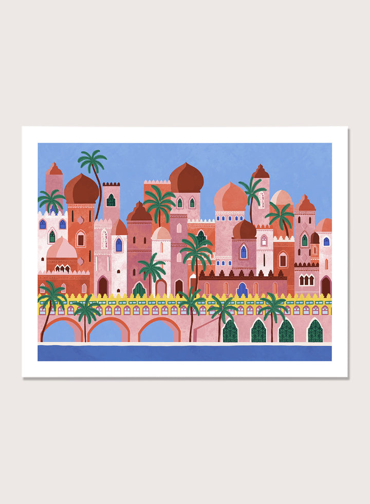 A framed art print featuring a stylized illustration of a coastal city with pink and peach buildings, green palm trees, and a blue sky. Arabian Fantasy City by Ceyda Alasar travel art print featuring ornate domes, arches, palm trees, patterned facades, and colorful desert architecture.