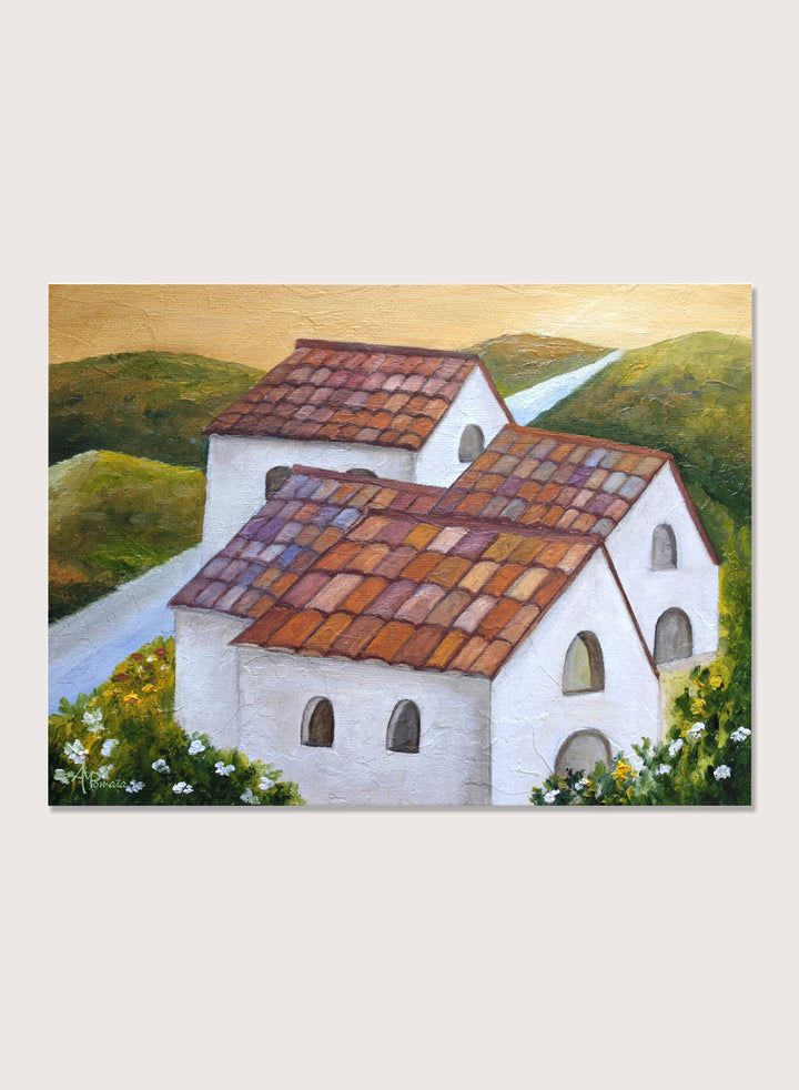A framed landscape painting depicting two white buildings with terracotta tiled roofs nestled in green hills, with a winding light blue road and a warm yellow sky. Shop Tuscan Hillside Village by Angeles M. Pomata, a warm countryside landscape art print featuring white houses, terracotta roofs, green hills, and wildflowers.