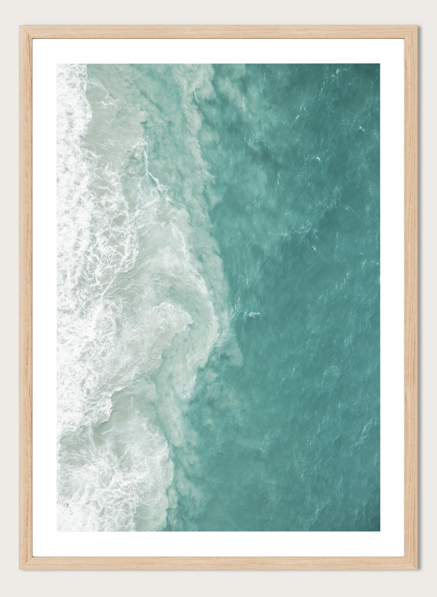 A framed aerial photograph of ocean waves, showing white foam breaking into turquoise and teal water. Ocean’s Edge by Shot by Clint aerial ocean photography print featuring turquoise water, white surf, and layered coastal movement.