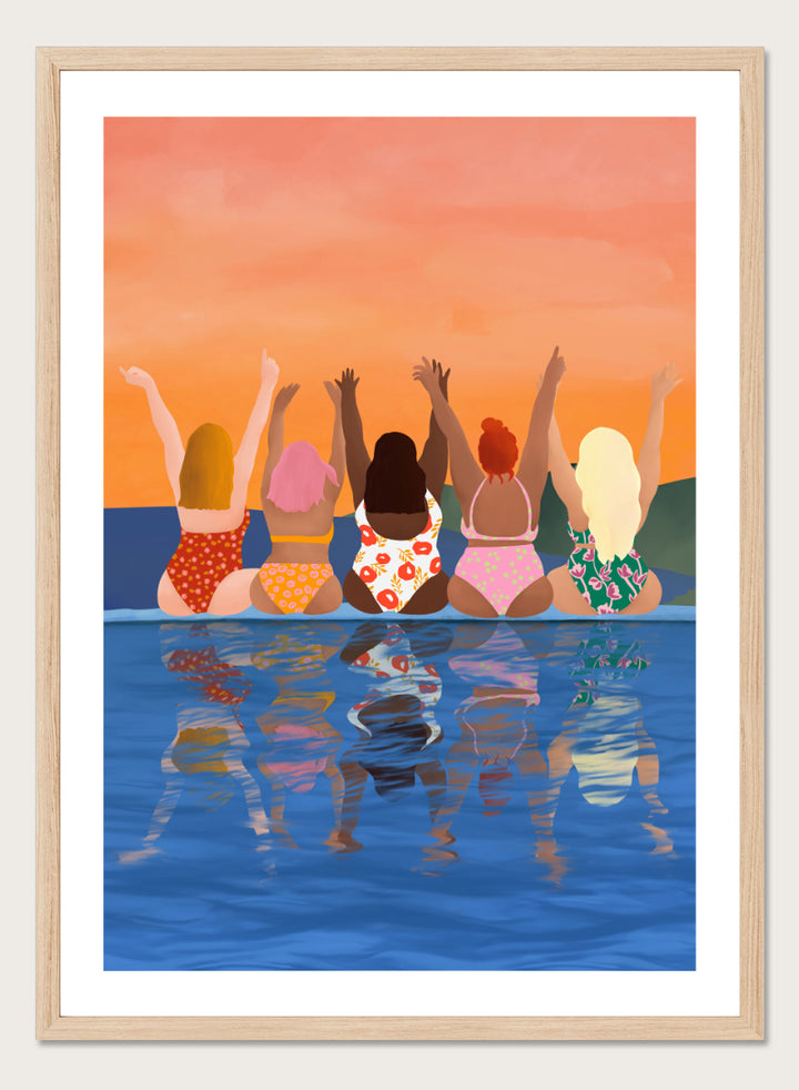 A framed art print featuring a stylized illustration of five women sitting in a pool at sunset, seen from behind as they raise their arms. The background is a warm orange sky, and the water below reflects their silhouettes. Summer Sunset Friends by Ceyda Alasar friendship art print featuring five women by the water in patterned swimsuits beneath a glowing orange sky.