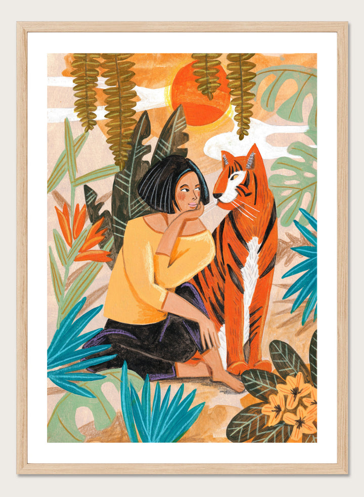 A framed art print featuring a stylized illustration of a woman in a yellow top and black skirt sitting beside an orange tiger, surrounded by tropical leaves and a warm orange sky. Woman with Tiger by Caroline Bonne Müller tropical art print featuring a woman beside a tiger among lush foliage, bold color, and hand-drawn texture.