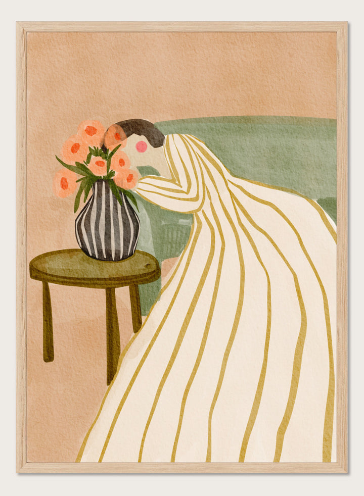 A stylized art print depicting a woman in a cream and gold striped gown leaning over a small table with a striped vase of pink flowers, set against a muted green sofa and beige background. Shop Woman Admiring Flowers by Nikita Jariwala, a modern floral wall art print featuring a woman, peach blooms, striped dress, and warm earthy tones.