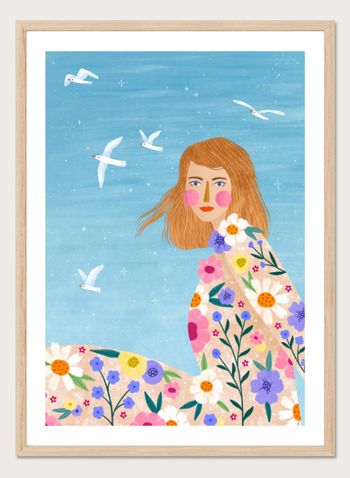 A framed art print featuring a stylized illustration of a young woman with long light brown hair, surrounded by colorful flowers and white birds against a light blue sky. ree Spirit Floral Dreams by Bea Müller floral woman art print featuring a flowing flower-covered summer dress, white birds, and a bright blue sky.