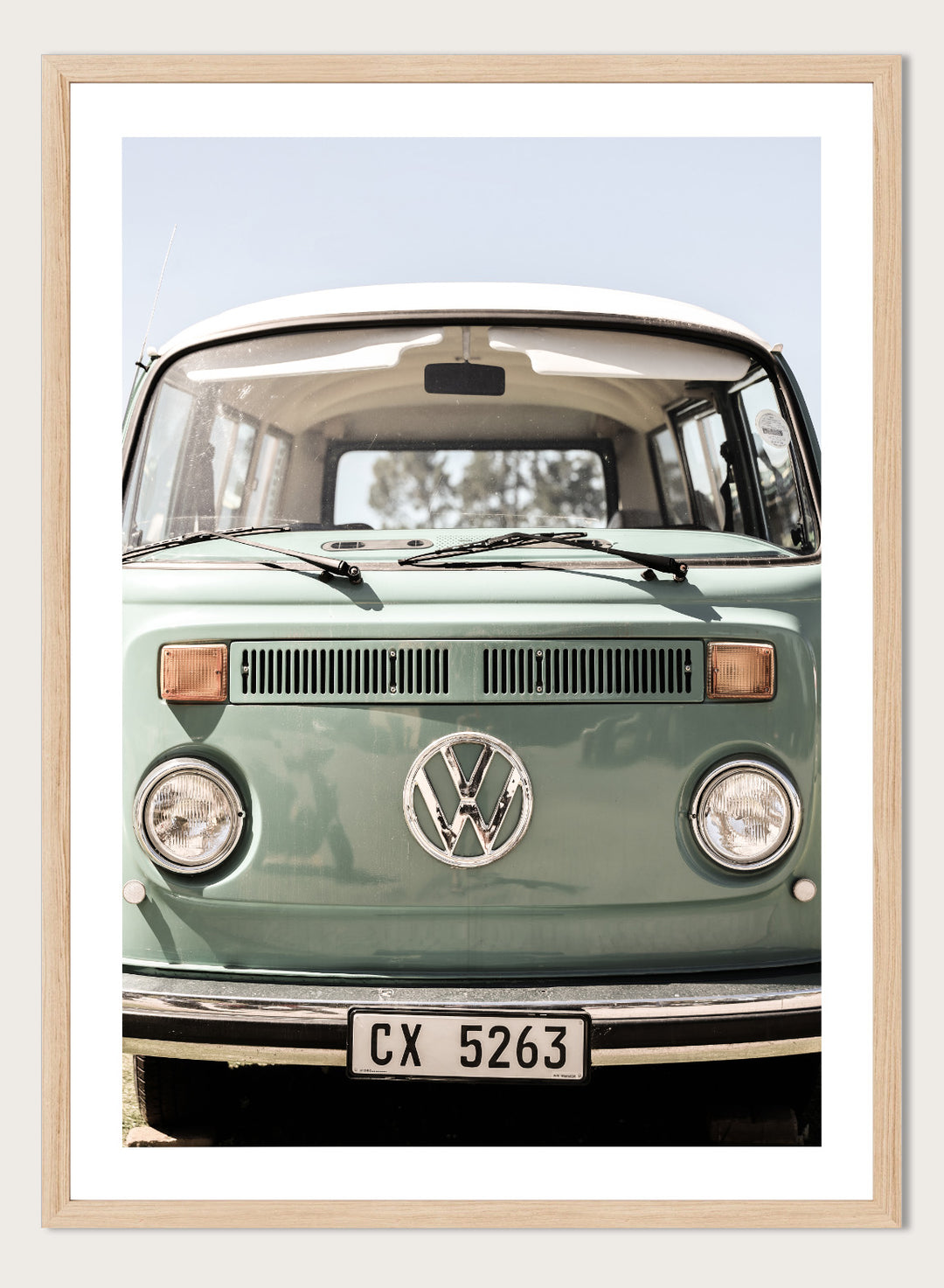 Front view of a vintage green Volkswagen van with clear sky background. Classic Design In Soft Green Tones by Shot by Clint car art print featuring a vintage Volkswagen camper van in soft sage green and warm sunlight.