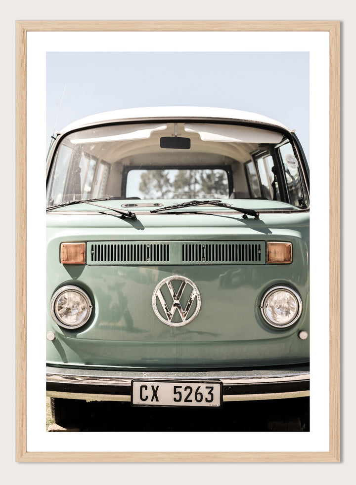 Front view of a vintage green Volkswagen van with clear sky background. Classic Design In Soft Green Tones by Shot by Clint car art print featuring a vintage Volkswagen camper van in soft sage green and warm sunlight.