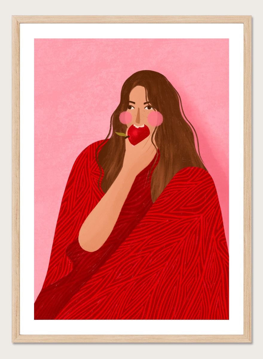 A framed art print featuring a stylized illustration of a woman with long brown hair, wearing a red patterned wrap, holding a red apple to her lips, set against a pink background. Cozy Woman Apple by Bea Müller portrait art print featuring a woman eating a red apple in bold red and pink tones for colorful modern wall decor.