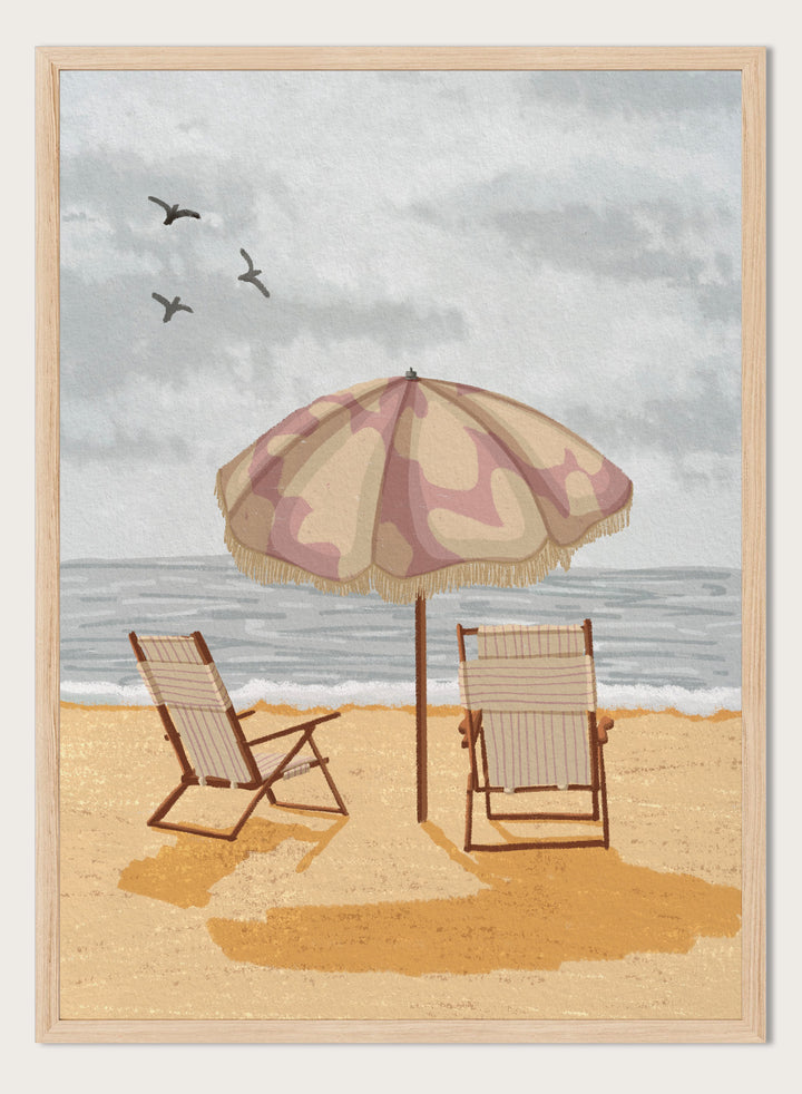 A beach scene artwork showing two wooden deck chairs under a beige and dusty pink patterned umbrella on a sandy shore, with the ocean and cloudy sky behind them. Two birds are visible in the sky. Seaside Umbrella Chairs by Lisa Solomoniuk premium framed fine art print featuring striped beach chairs beneath a fringed umbrella by the sea.