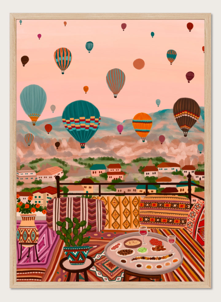 A colorful art print depicting a scenic view of a hillside town with mountains in the background, filled with hot air balloons. In the foreground, a patterned outdoor seating area features a table with food and a potted plant. Shop Balloons Over Rooftop Dinner by Nidhi Kachhadiya, a colorful travel wall art print featuring hot air balloons, rooftop dining, patterned textiles, and teal and coral tones.