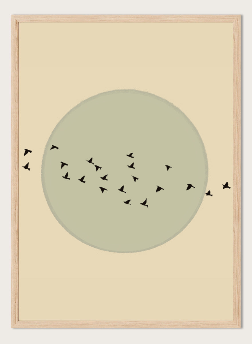 Minimalist art print featuring a large muted sage green circle centered on a warm beige background, with small black bird silhouettes flying around it. Flock Against The Moon by The Art Concept is a minimalist bird art print featuring black birds in flight across a pale green moon and warm cream background.