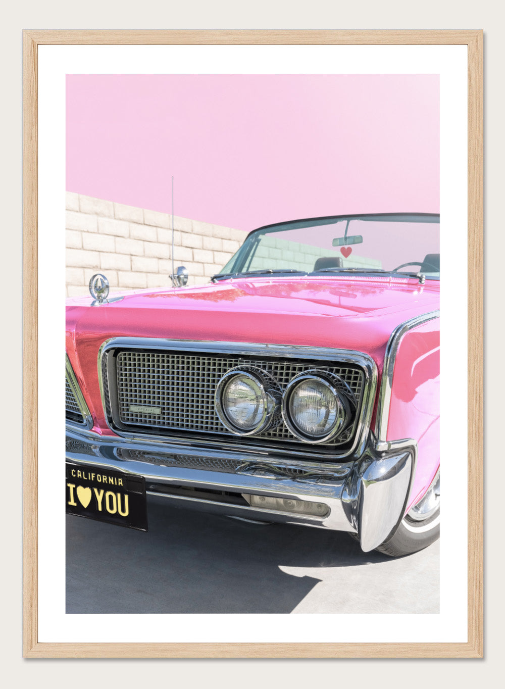 Pink vintage car with 'I ❤️ YOU' license plate against a pink sky. P.S. I Love You by Tom Windeknecht is officially licensed photography featuring a vibrant pop-art style photo of a car with romantic typography. Framed or unframed.