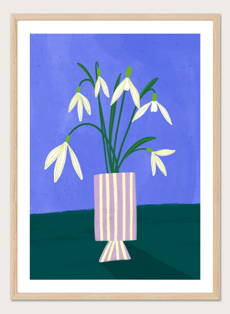 A framed art print featuring a stylized illustration of white snowdrops with green stems in a lavender and cream striped vase, set against a blue and dark green background. Snowdrops in Striped Vase by Bea Müller fine art print featuring white snowdrops, a lilac striped vase, and a deep blue background.