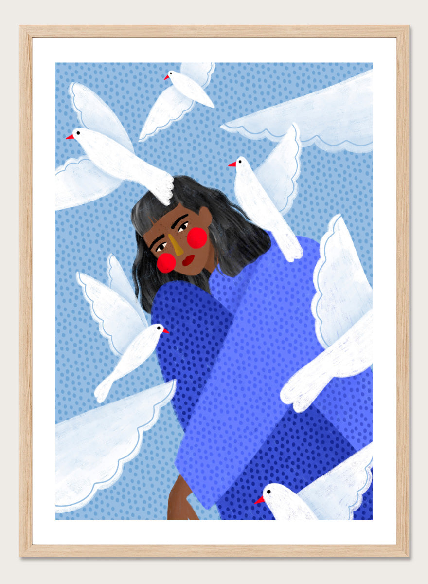 A framed art print featuring a stylized illustration of a woman with dark hair and red cheeks, wrapped in a blue patterned blanket, surrounded by white doves against a light blue dotted background. Peaceful Woman and Doves by Bea Müller art print featuring a woman in blue surrounded by white birds, layered textures, and soft modern color.