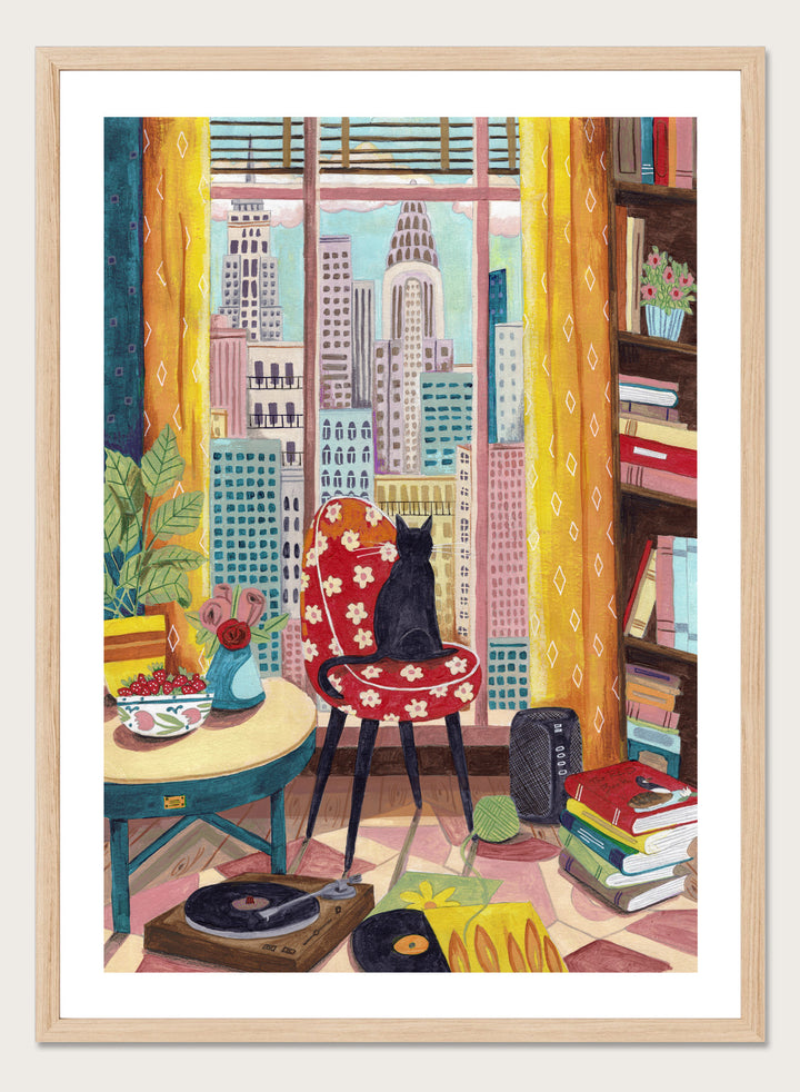 Colorful interior scene with a cat on a chair, books, and cityscape view. Black Cat City View by Caroline Bonne Müller is a fine art print and wall poster of a black cat by a window with city skyline and colorful interior.