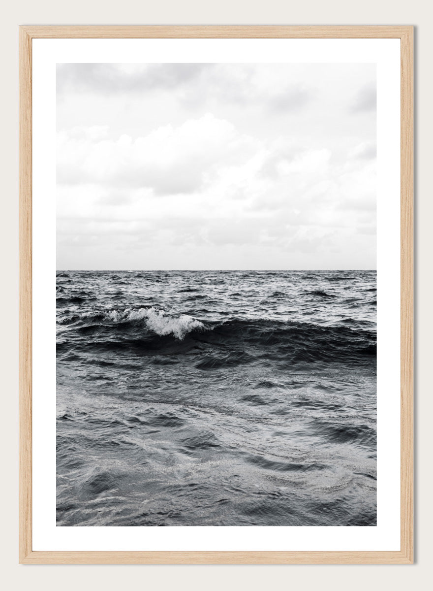 Black and white photographic art print of ocean waves under a cloudy sky. Endless Waves by Shot by Clint black-and-white ocean photography print featuring rolling water, textured surf, cloudy skies, and dramatic coastal movement.