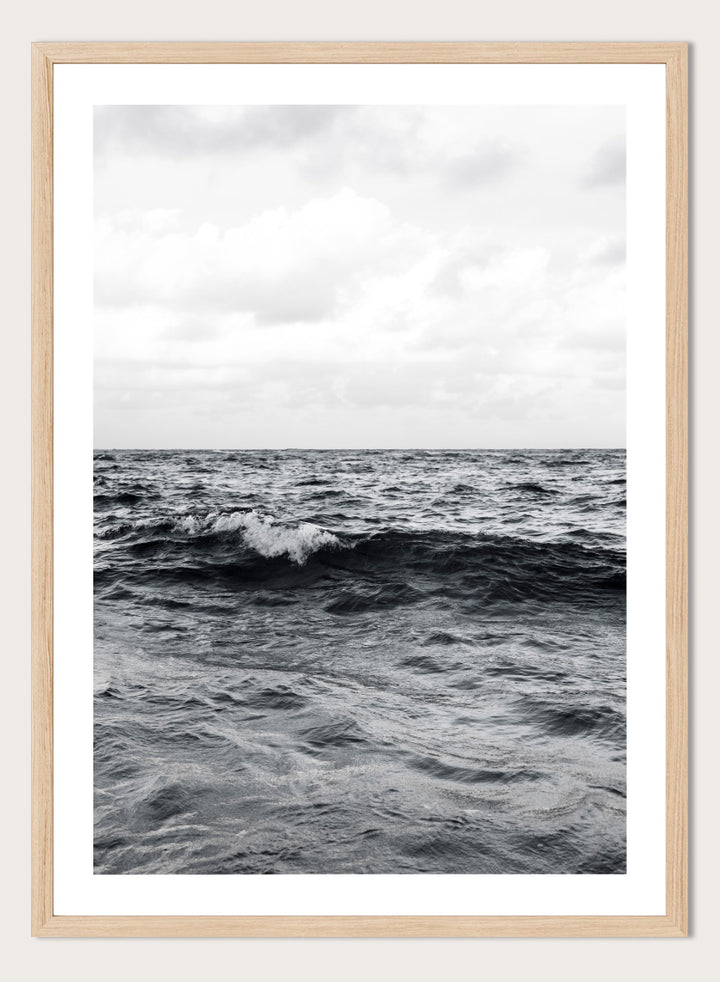 Black and white photographic art print of ocean waves under a cloudy sky. Endless Waves by Shot by Clint black-and-white ocean photography print featuring rolling water, textured surf, cloudy skies, and dramatic coastal movement.