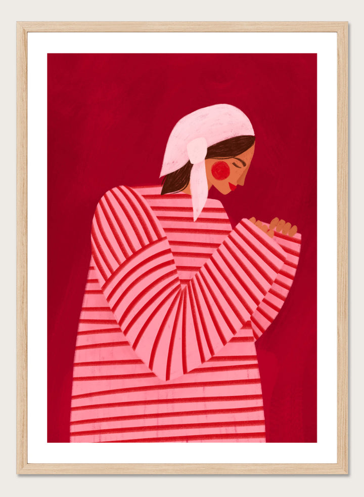A framed art print featuring a stylized illustration of a woman in a pink and red striped top and white headscarf against a deep red background. Serene Praying Woman by Bea Müller portrait art print featuring a reflective woman in a pink striped dress against a rich red background.