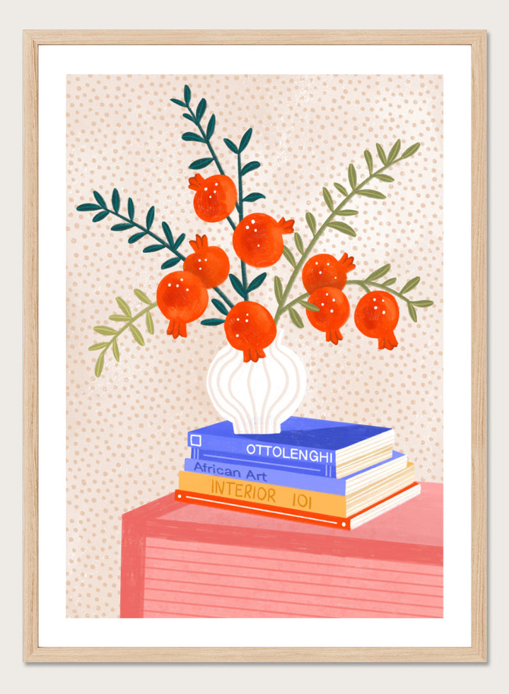 A framed art print featuring a stylized illustration of pomegranate branches in a white vase resting on a stack of books, set against a light beige dotted background. Cozy Tabletop Pomegranates by Bea Müller still life art print featuring red fruit branches, a sculptural vase, design books, and colorful interior styling.