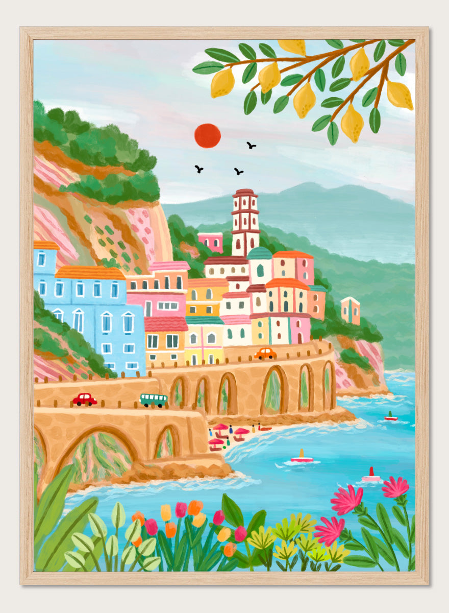 A colorful illustrated coastal town scene with pastel buildings, a stone bridge, blue water, mountains, flowers, and hanging yellow leaves. Shop Colorful Amalfi Coast by Nidhi Kachhadiya, a vibrant Italian coastal wall art print inspired by the Amalfi Coast, pastel villages, blue sea, and lemon trees.