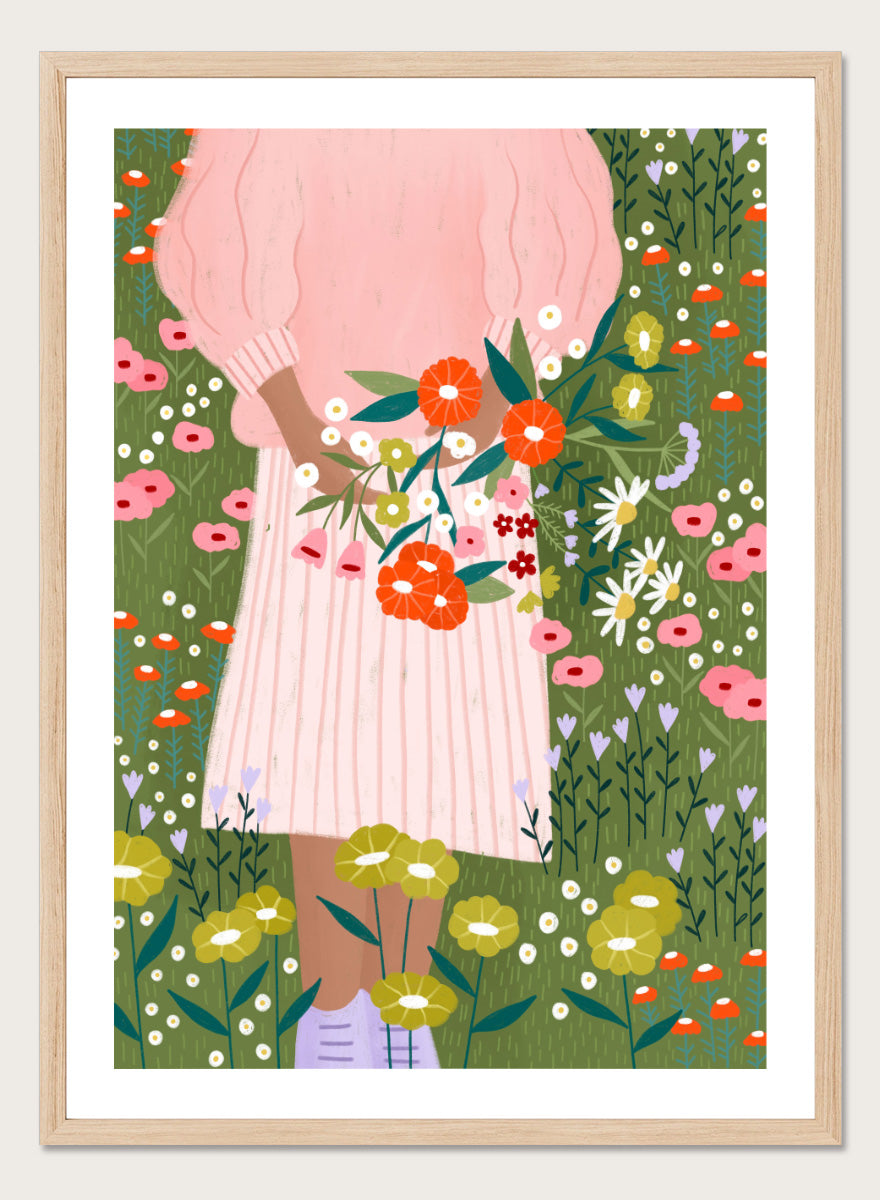 A framed art print featuring a stylized illustration of a person in a pink striped dress holding a bouquet of orange, red, and white flowers in a green field of wildflowers. Secret Garden Bouquet by Bea Müller floral art print featuring a woman gathering wildflowers in a colorful garden filled with poppies, daisies, and greenery.
