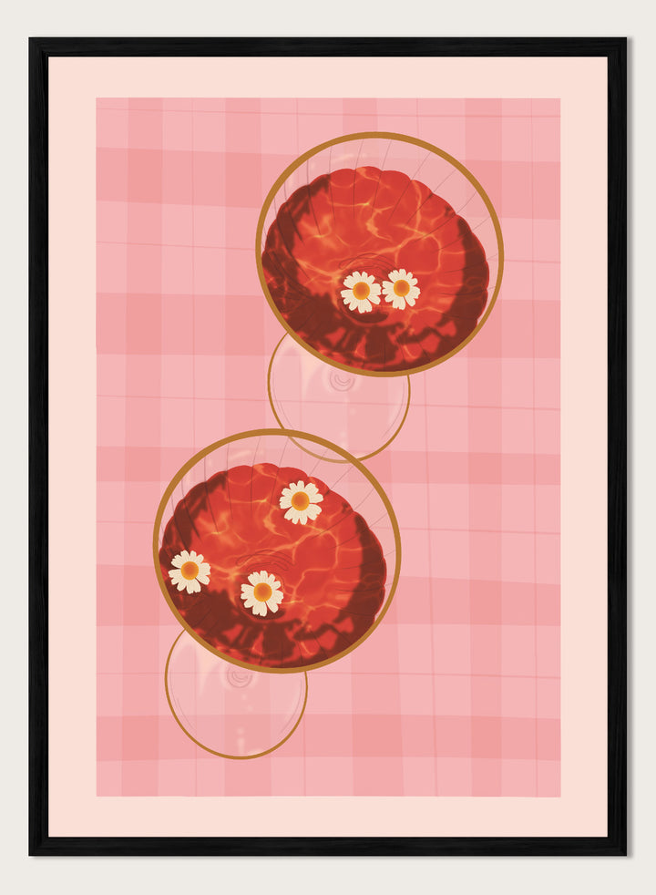 A stylized art print featuring two overlapping pink and red plaid glasses with white daisy flowers, framed by a black border on a light pink background. Pink Drinks With Daisies by Lisa Solomoniuk premium framed fine art print featuring red coupe glasses, floating daisies, and pink gingham.