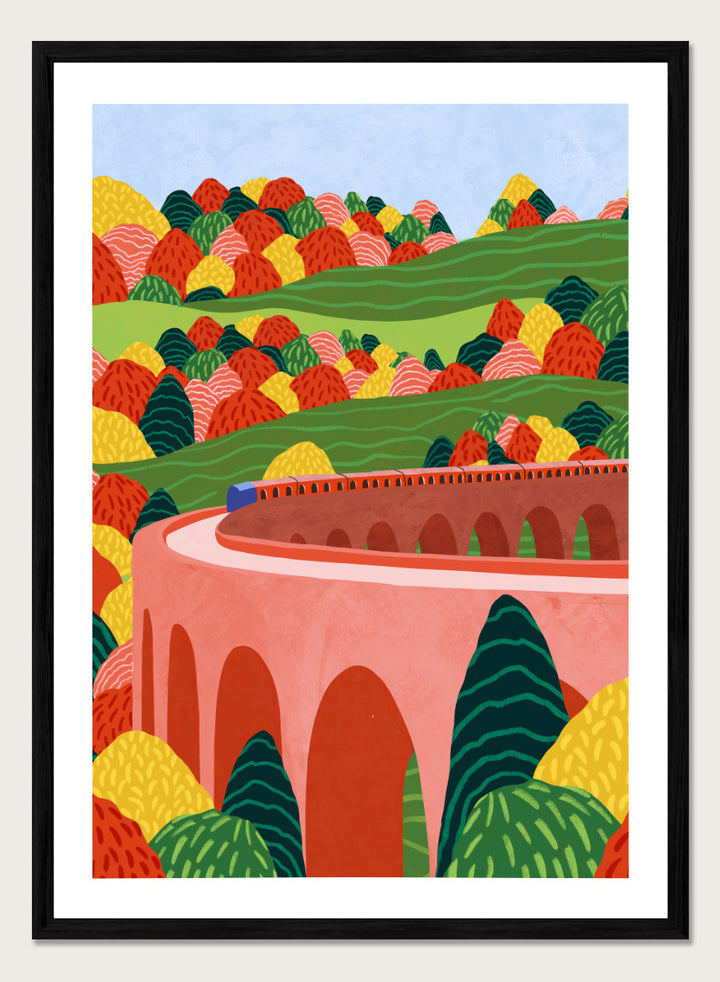 A framed art print featuring a stylized landscape illustration with rolling green hills, colorful patterned trees, and a pink arch bridge under a light blue sky. Winding Autumn Viaduct by Ceyda Alasar travel art print featuring a colorful train, arched bridge, rolling hills, and bold autumn foliage.