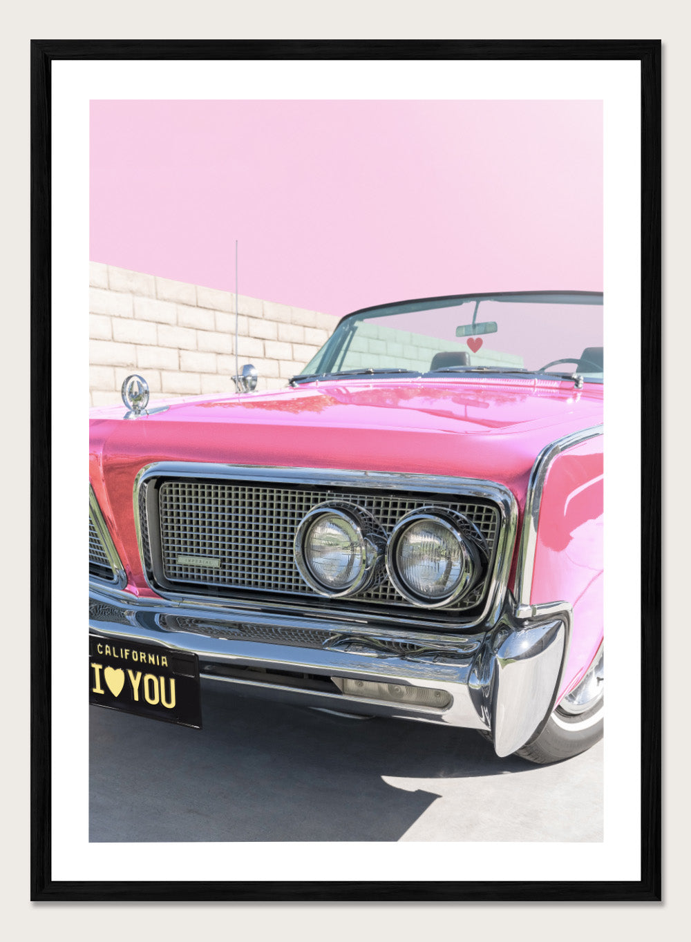 Pink vintage car with 'I ❤️ YOU' license plate against a pink sky. P.S. I Love You by Tom Windeknecht is officially licensed photography featuring a vibrant pop-art style photo of a car with romantic typography. Framed or unframed.