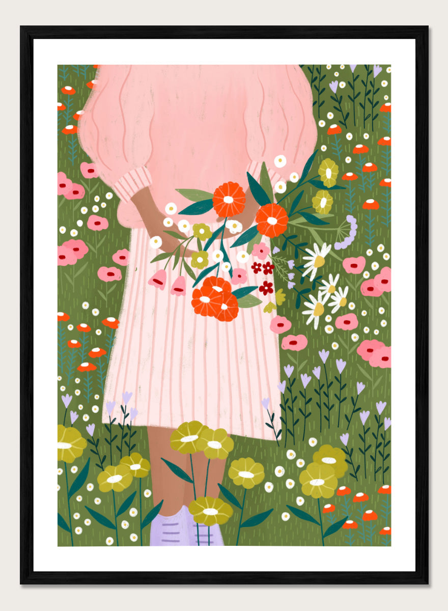 A framed art print featuring a stylized illustration of a person in a pink striped dress holding a bouquet of orange, red, and white flowers in a green field of wildflowers. Secret Garden Bouquet by Bea Müller floral art print featuring a woman gathering wildflowers in a colorful garden filled with poppies, daisies, and greenery.