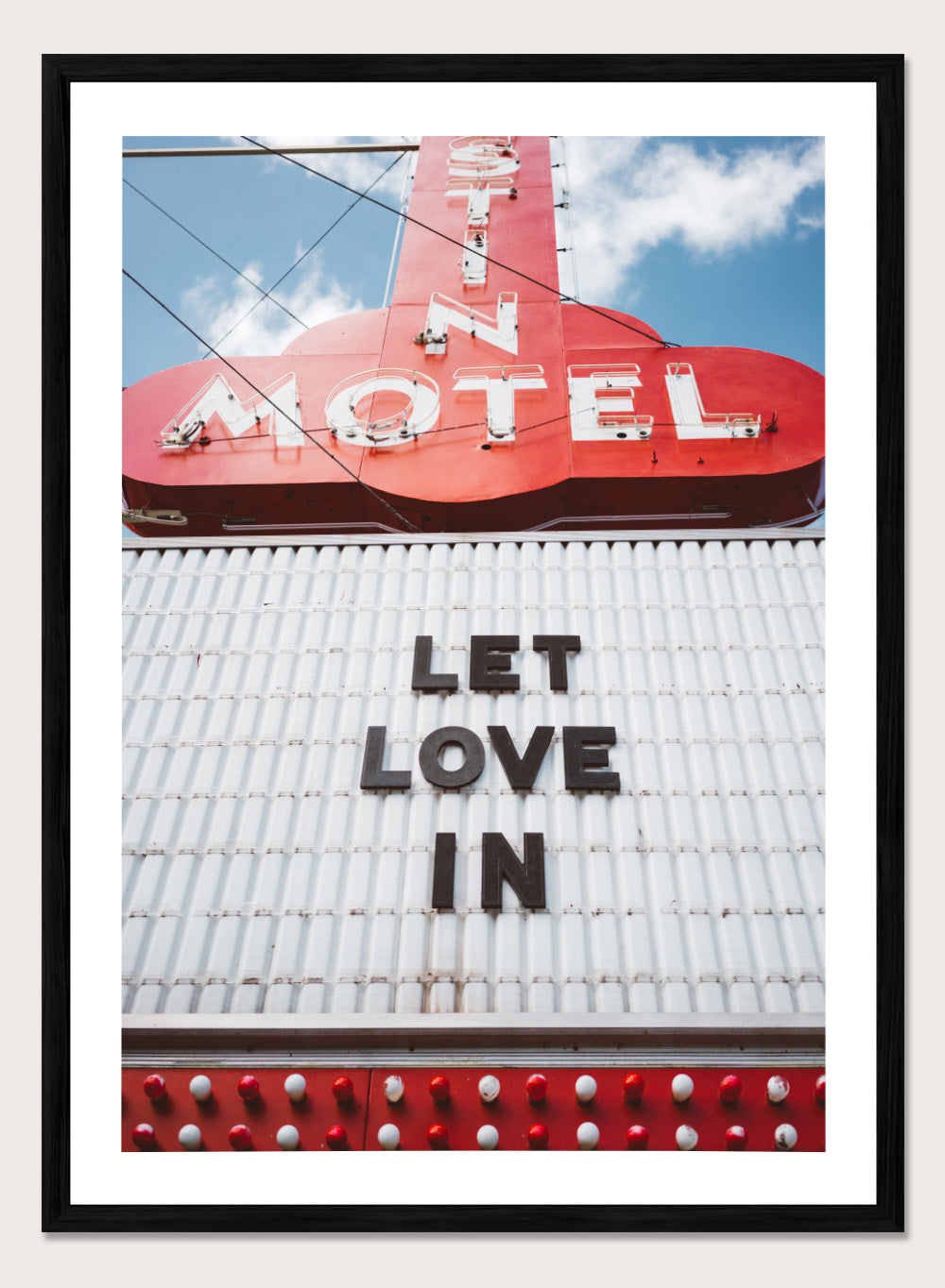 Vintage motel sign with 'Let Love In' message against a blue sky. Let Love In by Bethany Young features a vintage motel sign with red neon lettering against blue sky. Retro Americana photography wall art print.