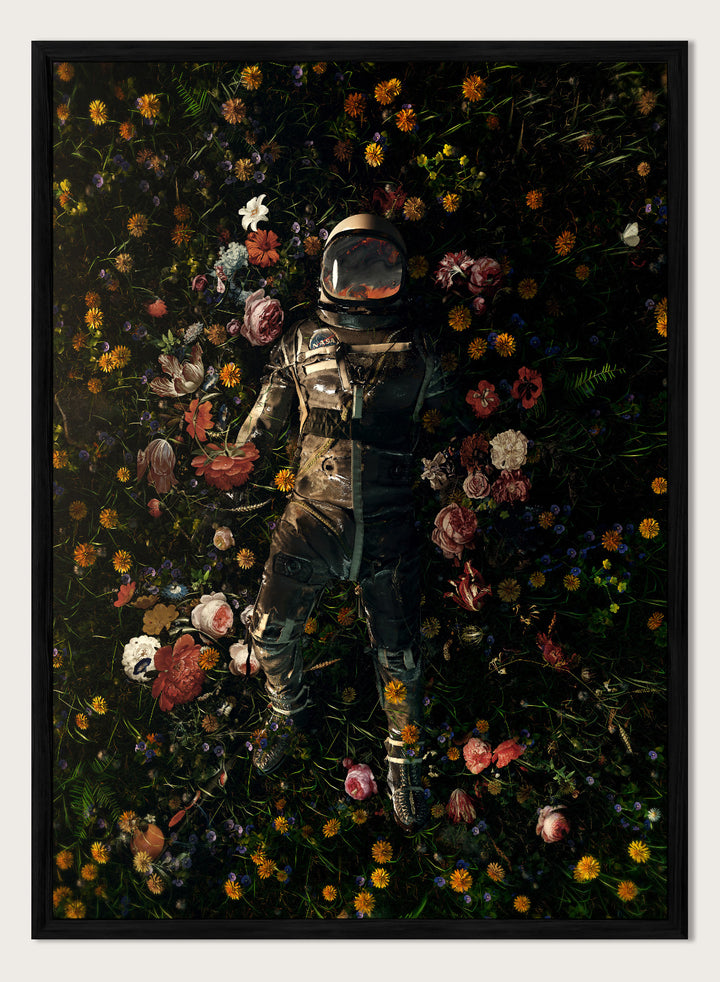 Person in a spacesuit lying on a bed of flowers with a dark background. Cosmic Floral Dream by Nicebleed is a surreal astronaut floral art print featuring a space figure surrounded by flowers, modern aesthetic wall poster.