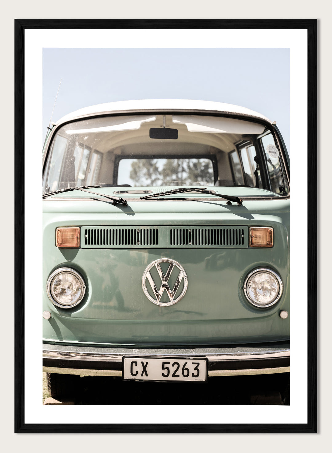 Front view of a vintage green Volkswagen van with clear sky background. Classic Design In Soft Green Tones by Shot by Clint car art print featuring a vintage Volkswagen camper van in soft sage green and warm sunlight.