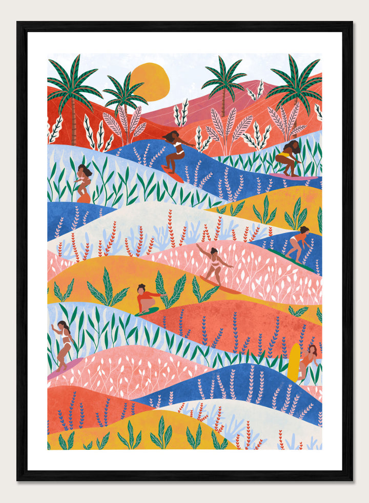 A framed art print featuring a colorful, stylized landscape illustration with rolling hills, palm trees, a sun, and small human figures in a folk-art style. Tropical Surf Girls by Ceyda Alasar surf art print featuring women riding waves through a colorful palm-filled landscape in bold tropical tones.