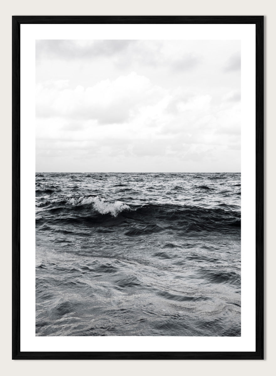 Black and white photographic art print of ocean waves under a cloudy sky. Endless Waves by Shot by Clint black-and-white ocean photography print featuring rolling water, textured surf, cloudy skies, and dramatic coastal movement.