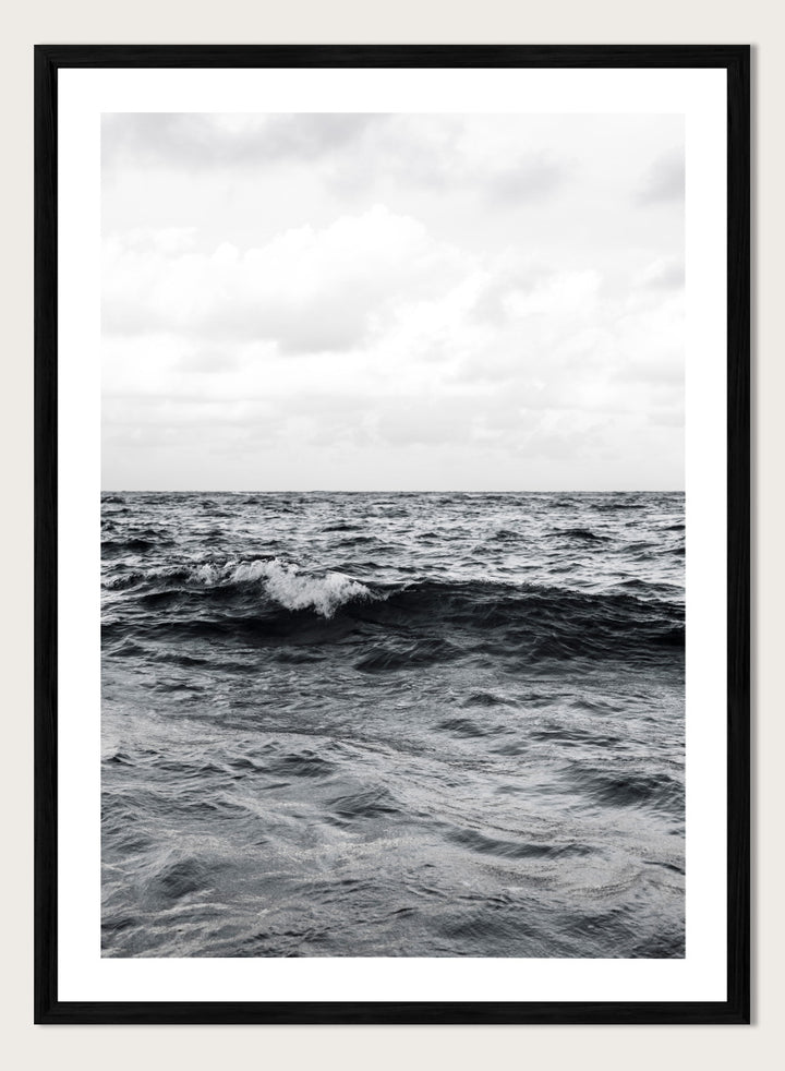 Black and white photographic art print of ocean waves under a cloudy sky. Endless Waves by Shot by Clint black-and-white ocean photography print featuring rolling water, textured surf, cloudy skies, and dramatic coastal movement.