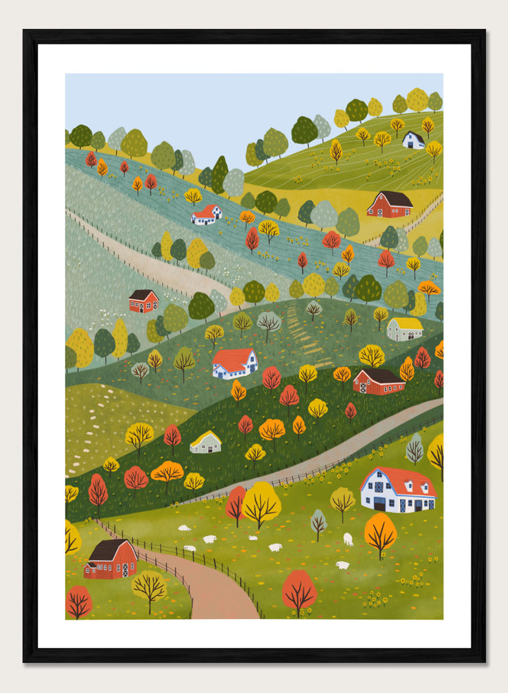 A framed art print featuring a whimsical, stylized illustration of a rolling green and yellow countryside landscape with red houses, colorful autumn trees, winding roads, and a pale blue sky. Vibrant Autumn Village Hills by Ceyda Alasar art print with rolling countryside, colorful fall trees, farmhouses, barns, sheep, and winding roads.