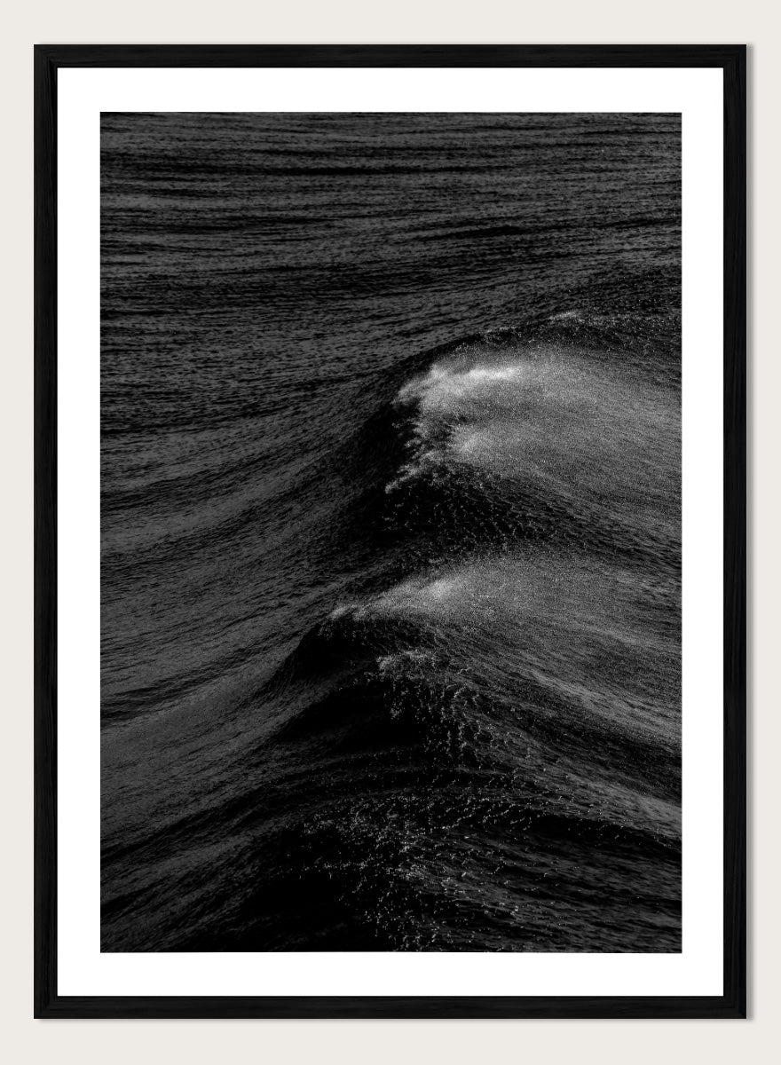Black and white fine art photographic print of ocean waves, featuring a dramatic wave crest with white foam against dark textured water. Night Wave Cascade by Shot by Clint black-and-white ocean photography print featuring dark rolling waves, sea spray, and dramatic natural movement.