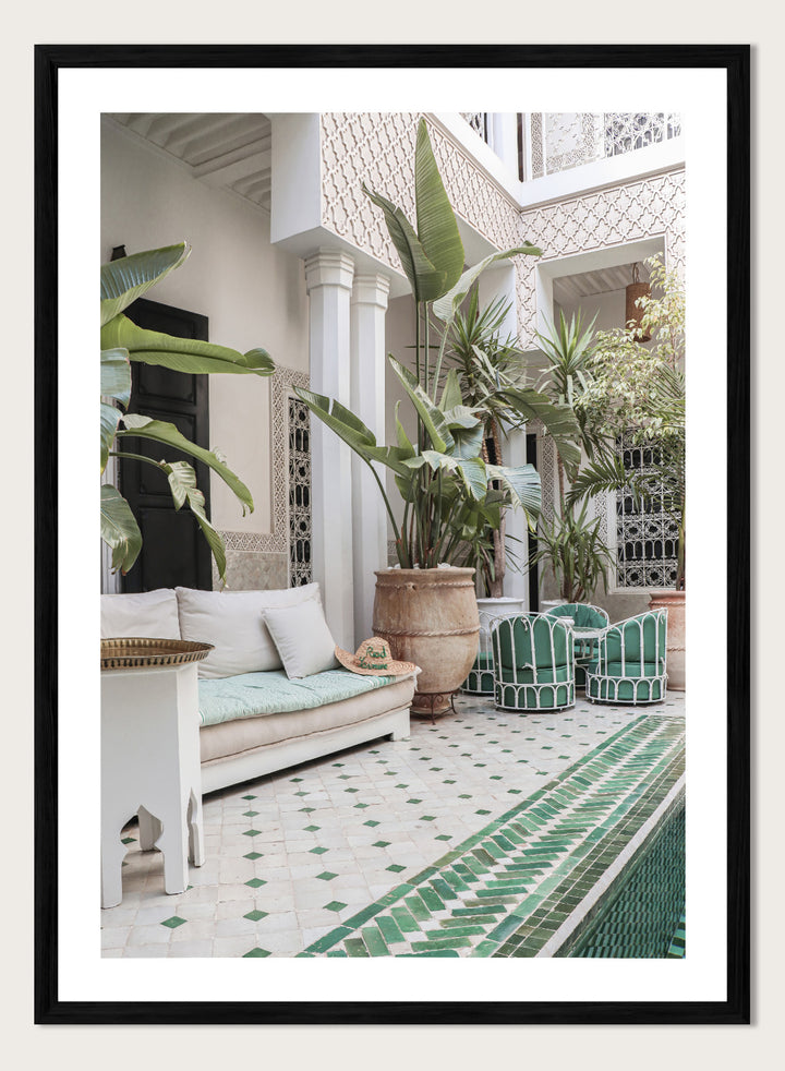 Outdoor patio with white sofa, green chairs, and potted plants in a decorative courtyard. Moroccan Riad Courtyard Oasis by Henrike Schenk is a Morocco photography print of a riad courtyard with tropical plants, tilework, and interior decor.