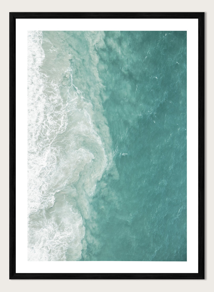 A framed aerial photograph of ocean waves, showing white foam breaking into turquoise and teal water. Ocean’s Edge by Shot by Clint aerial ocean photography print featuring turquoise water, white surf, and layered coastal movement.